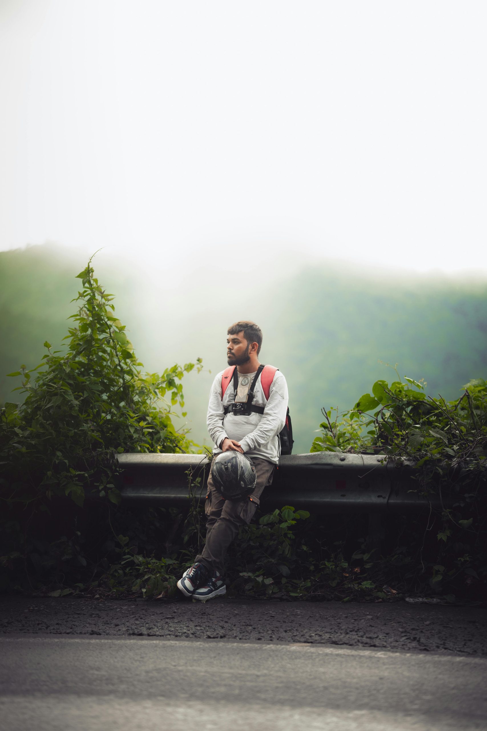 A man with a backpack enjoying a moment of rest by a misty mountain roadside in Chhattisgarh, India.